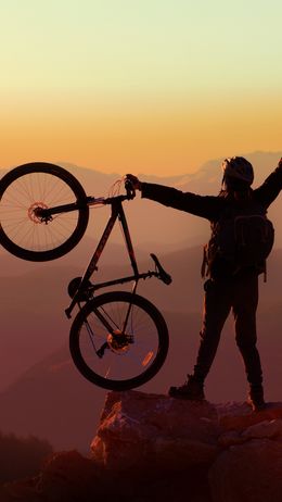 Silhouette eines Bikers mit Fahrrad auf Felsen bei Sonnenaufgang